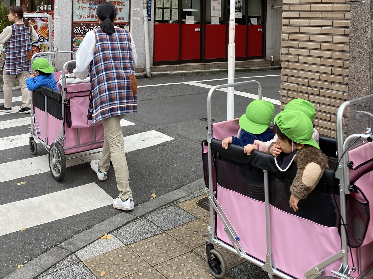 保育士が、カートに乗った小さな子どもたちと東京の町を散歩している
